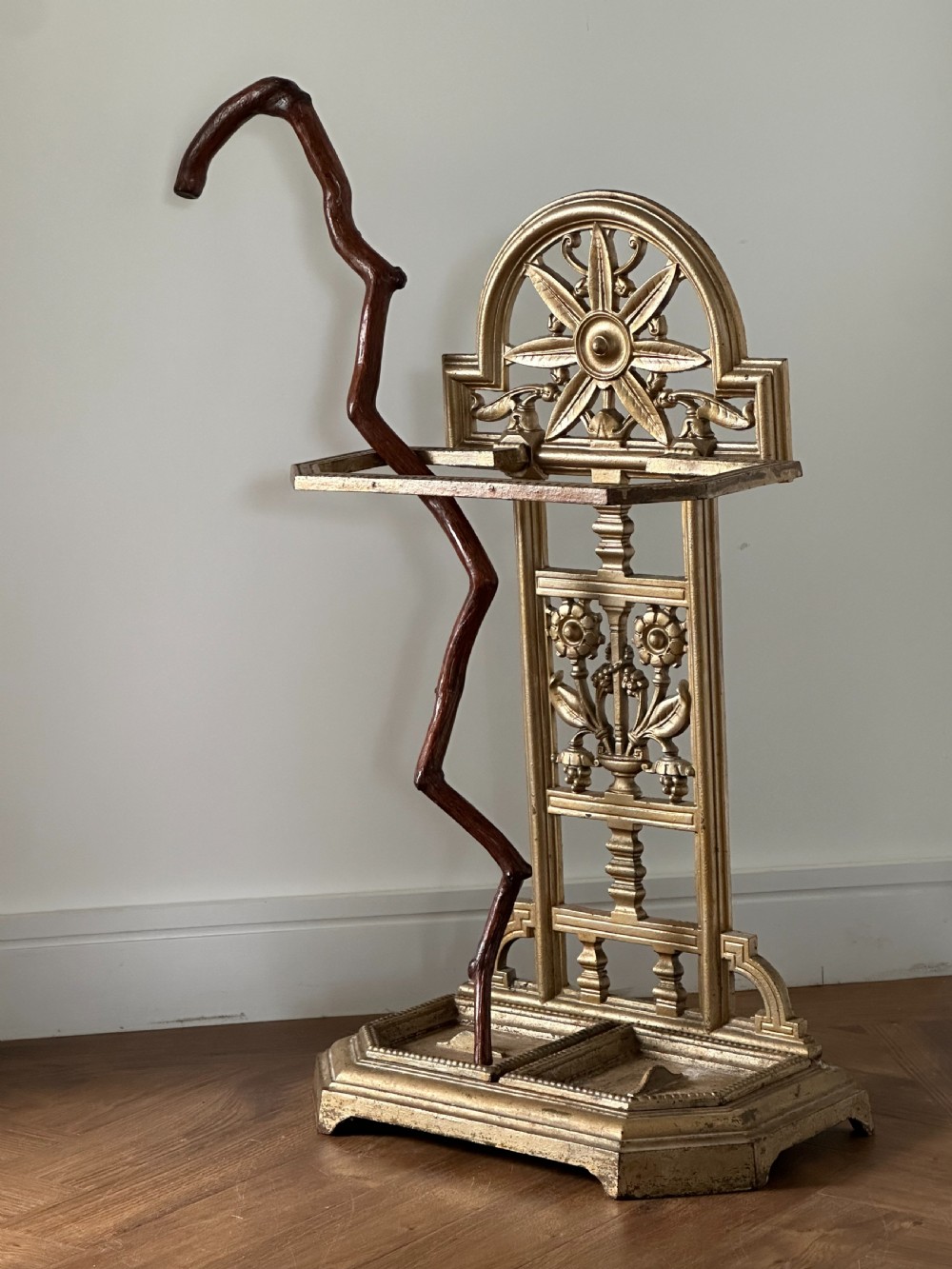 A gold-painted cast iron stick stand featuring a starburst arched cresting, stylised floral central panel, rectangular top ring, and a heavy drip tray base. View II