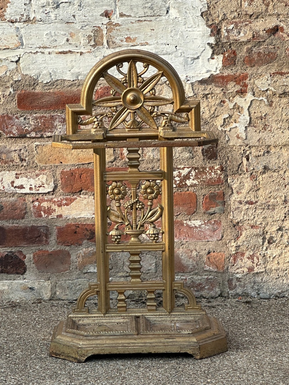 A gold-painted cast iron stick stand featuring a starburst arched cresting, stylised floral central panel, rectangular top ring, and a heavy drip tray base. View IX