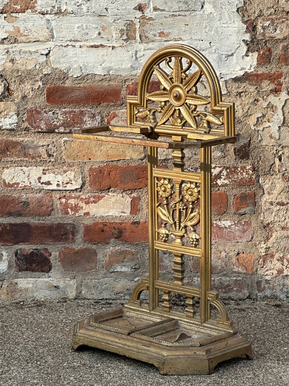 A gold-painted cast iron stick stand featuring a starburst arched cresting, stylised floral central panel, rectangular top ring, and a heavy drip tray base.