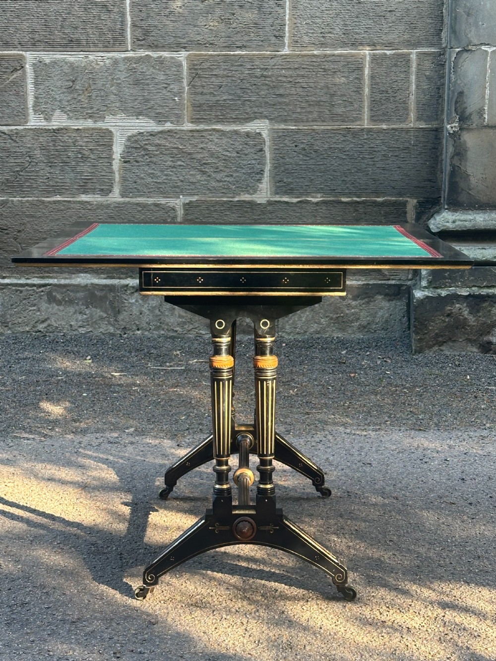 A late Victorian ebonised and parcel gilt card table with a green baize top and turned amboyna columns.