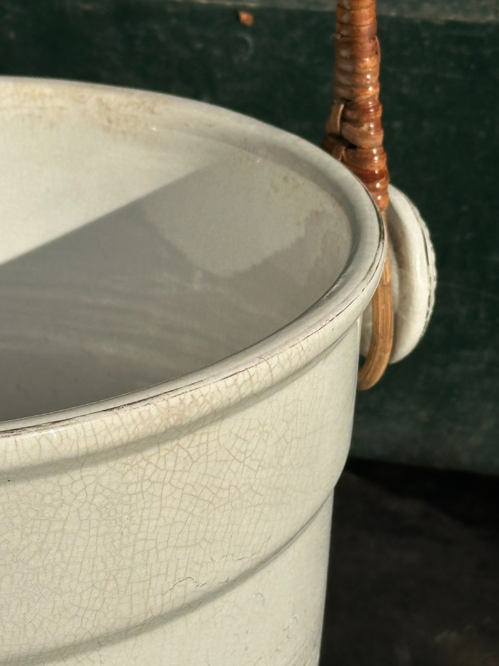 A cream-glazed ceramic bucket featuring a horizontal gilt line and a cane-wrapped overhead swing handle. View II