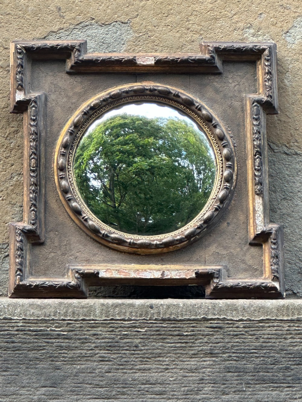 A late 19th-century square dark wood wall mirror featuring stepped architectural outer corners and a central gilt-trimmed circular convex mirror.