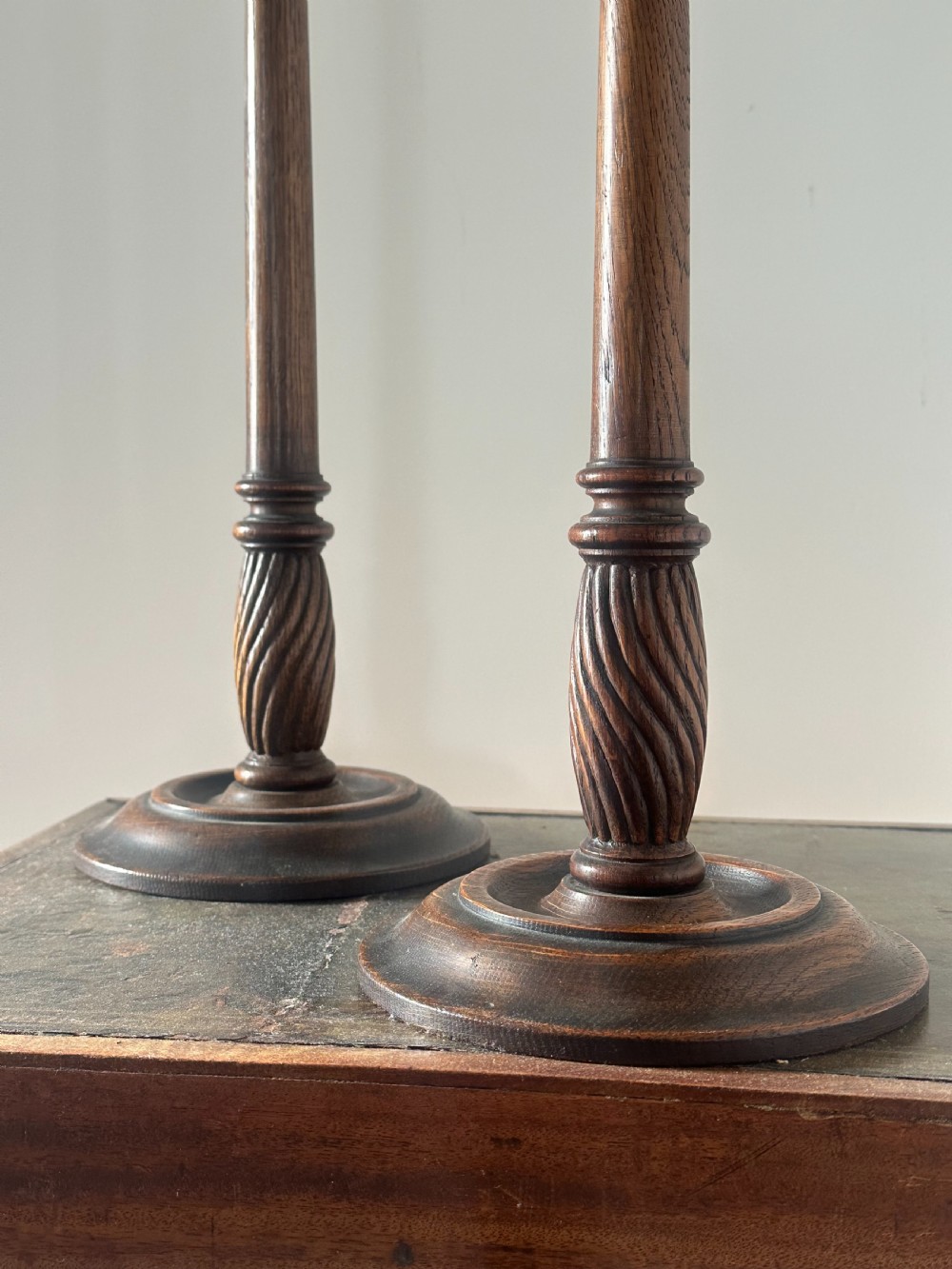 A pair of tall turned dark oak candlesticks with spiral-carved columns, circular bases, and brass sconces holding red tapered candles. View V