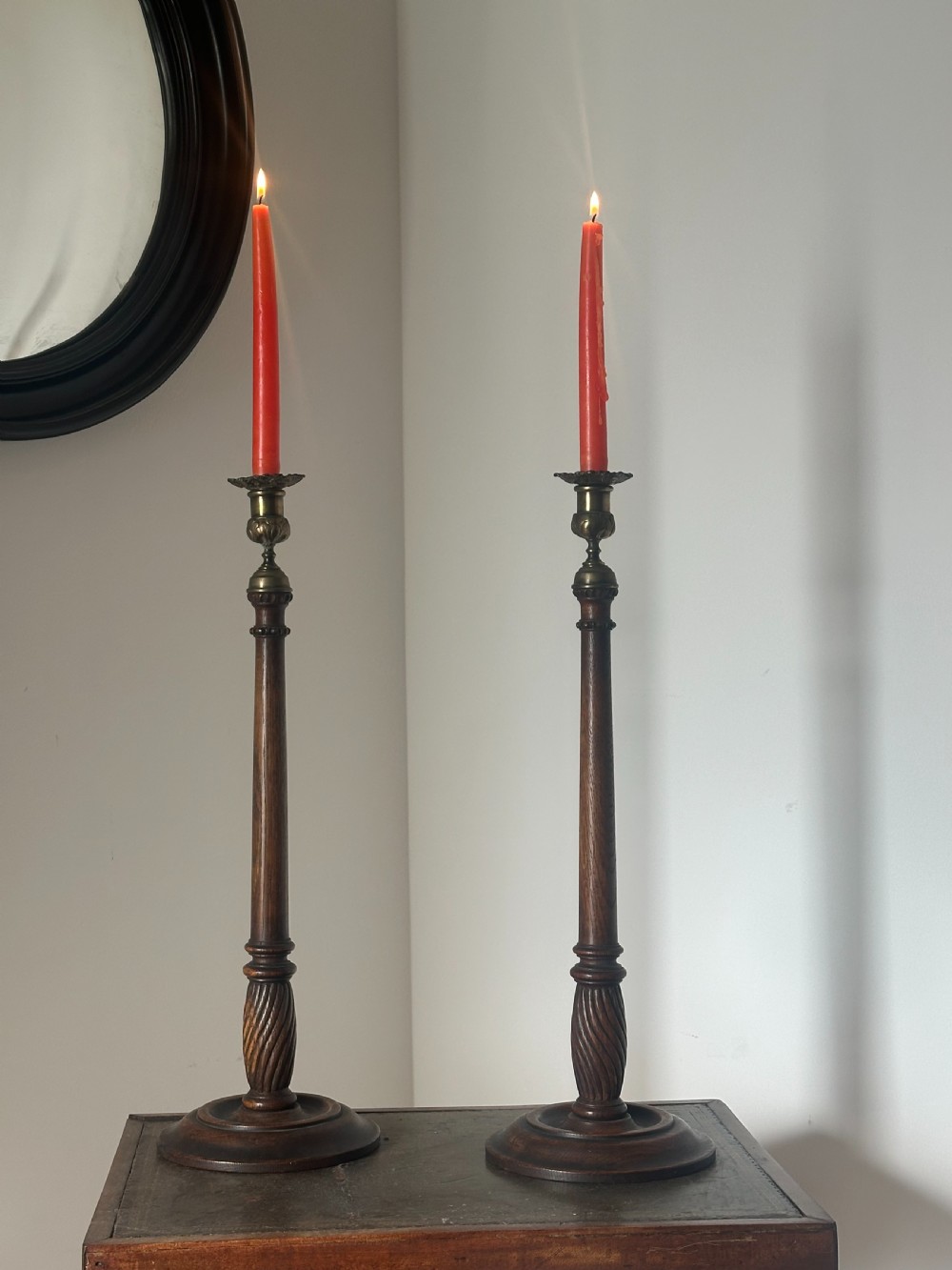 A pair of tall turned dark oak candlesticks with spiral-carved columns, circular bases, and brass sconces holding red tapered candles.