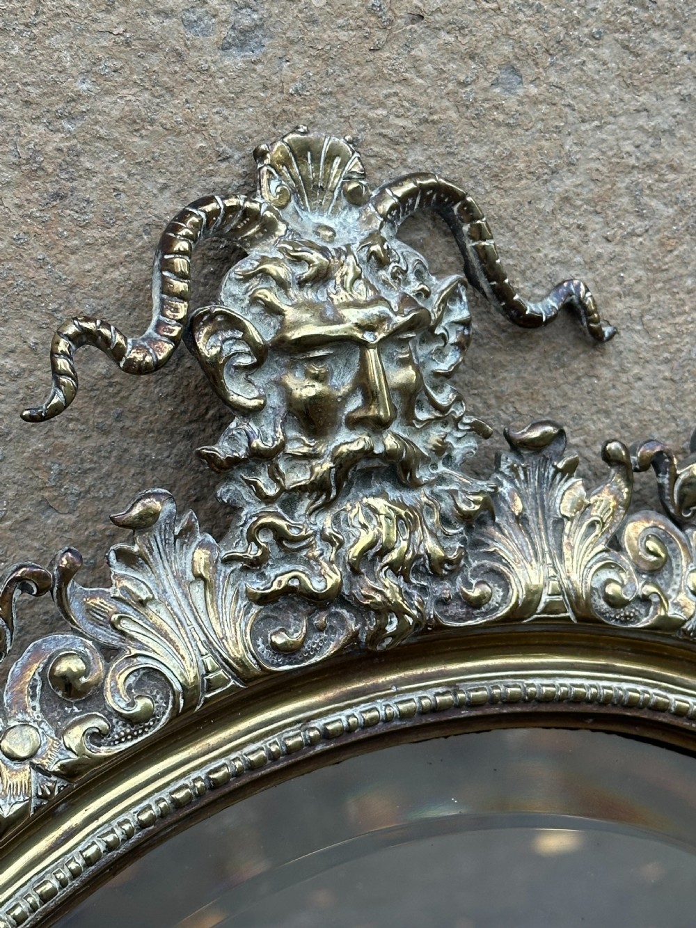 A circular Victorian cast brass wall mirror featuring a detailed crest with a mythological mask motif and a bevelled glass plate. View II