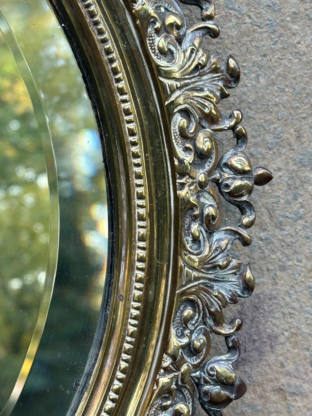 A circular Victorian cast brass wall mirror featuring a detailed crest with a mythological mask motif and a bevelled glass plate. View III