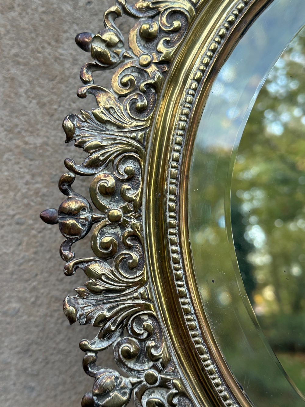 A circular Victorian cast brass wall mirror featuring a detailed crest with a mythological mask motif and a bevelled glass plate. View IV