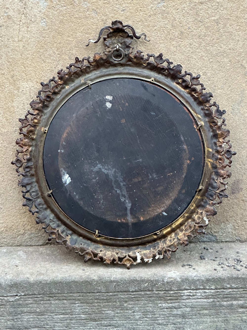 A circular Victorian cast brass wall mirror featuring a detailed crest with a mythological mask motif and a bevelled glass plate. View V