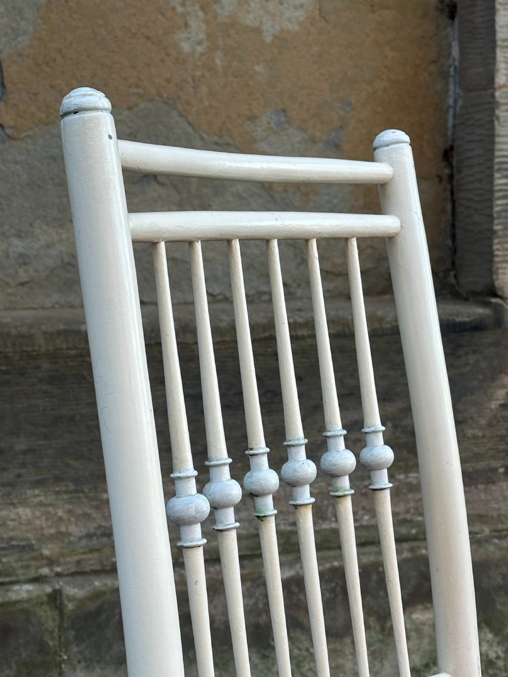 A white painted Arts and Crafts armchair with a tall spindle back, straight arms, and a padded red fabric seat secured with brass studs. View II