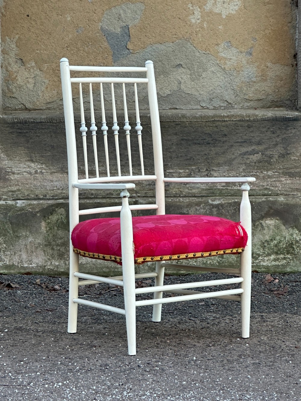 A white painted Arts and Crafts armchair with a tall spindle back, straight arms, and a padded red fabric seat secured with brass studs. View III