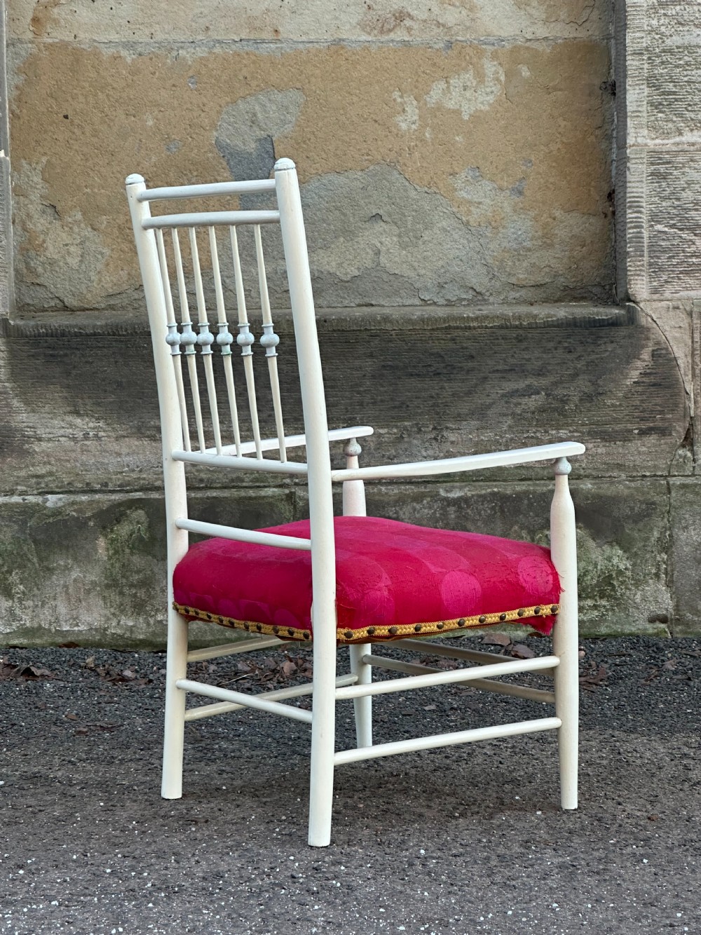 A white painted Arts and Crafts armchair with a tall spindle back, straight arms, and a padded red fabric seat secured with brass studs. View IV