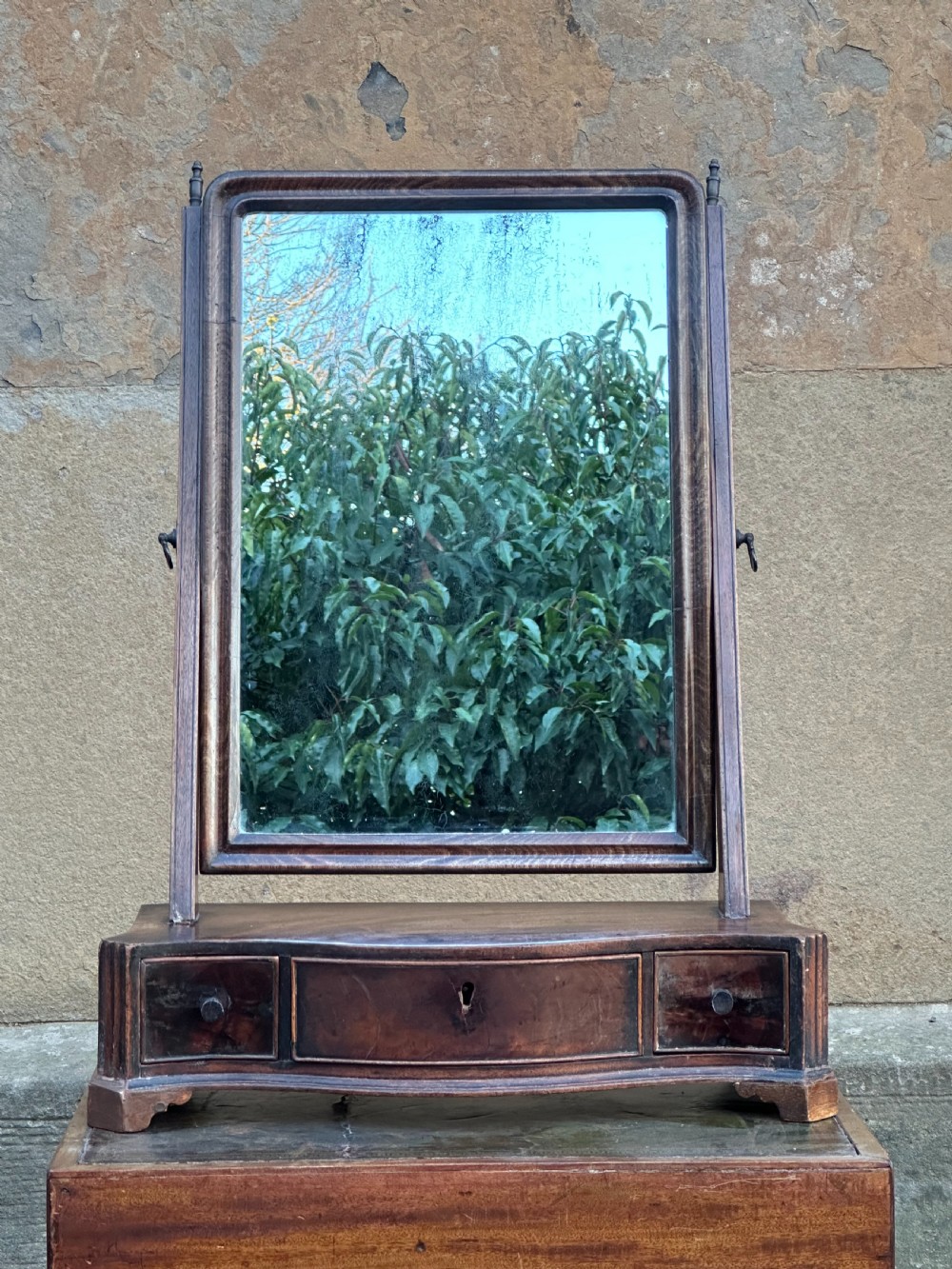 A mid-18th-century George II mahogany toilet mirror with a rectangular swing glass supported by side uprights above a drawers base.