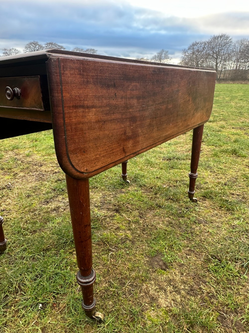 A Scottish Regency dark mahogany dining table featuring turned legs ending in brass castors and an integrated end drawer. View III