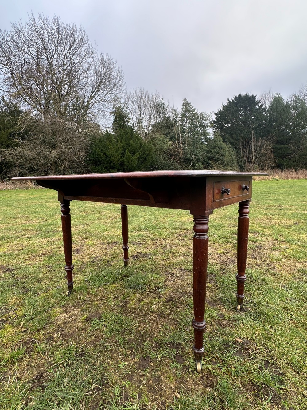 A Scottish Regency dark mahogany dining table featuring turned legs ending in brass castors and an integrated end drawer.
