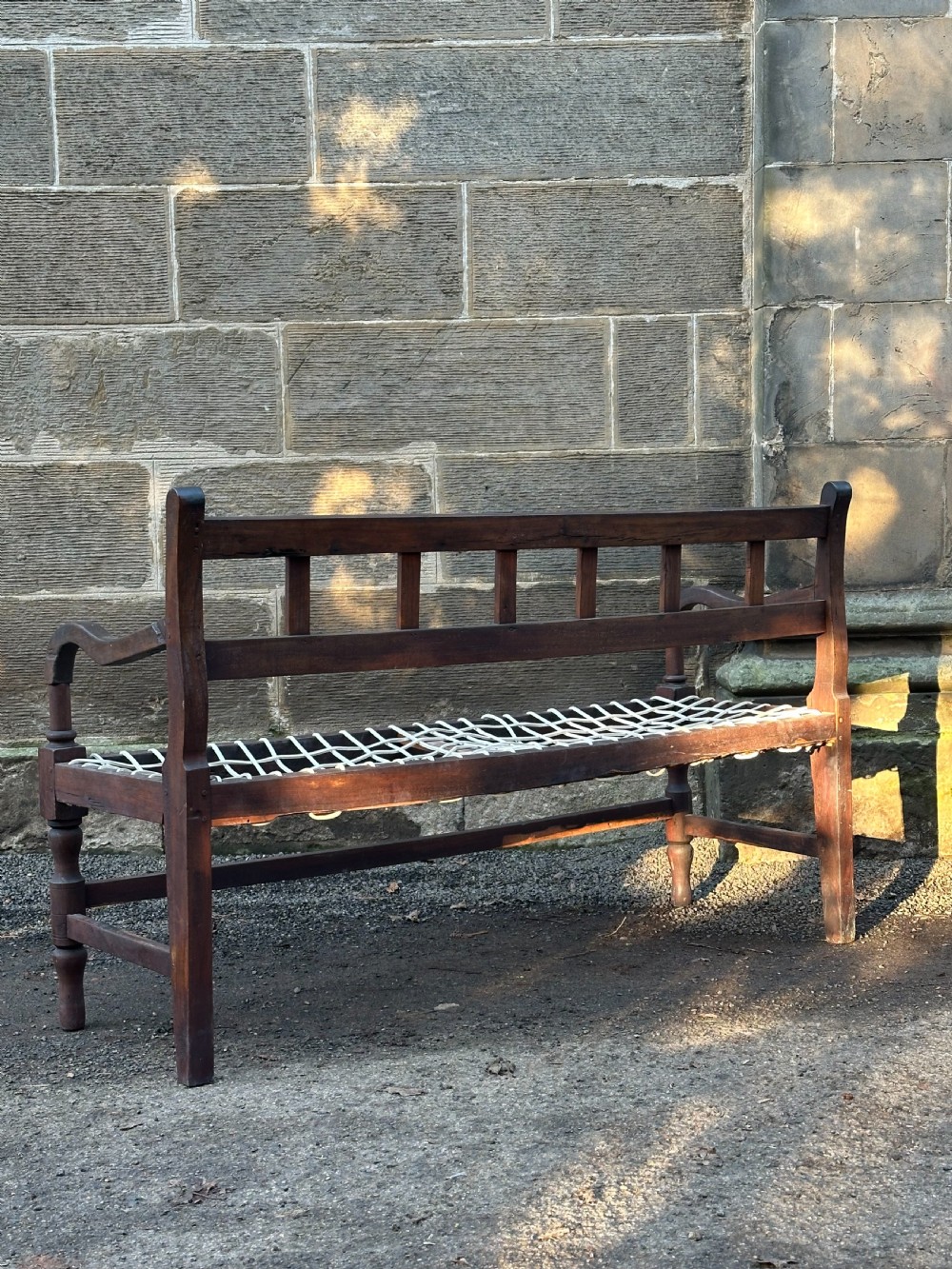 An early 19th-century South African stinkwood bench featuring a woven leather thong seat, curved armrests, and turned front legs. View II