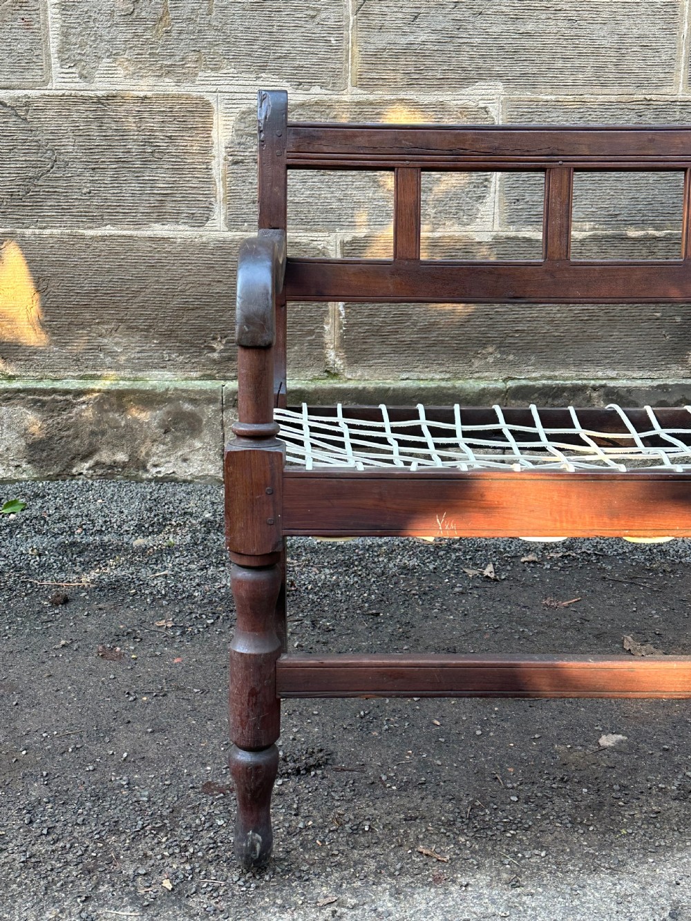 An early 19th-century South African stinkwood bench featuring a woven leather thong seat, curved armrests, and turned front legs. View III