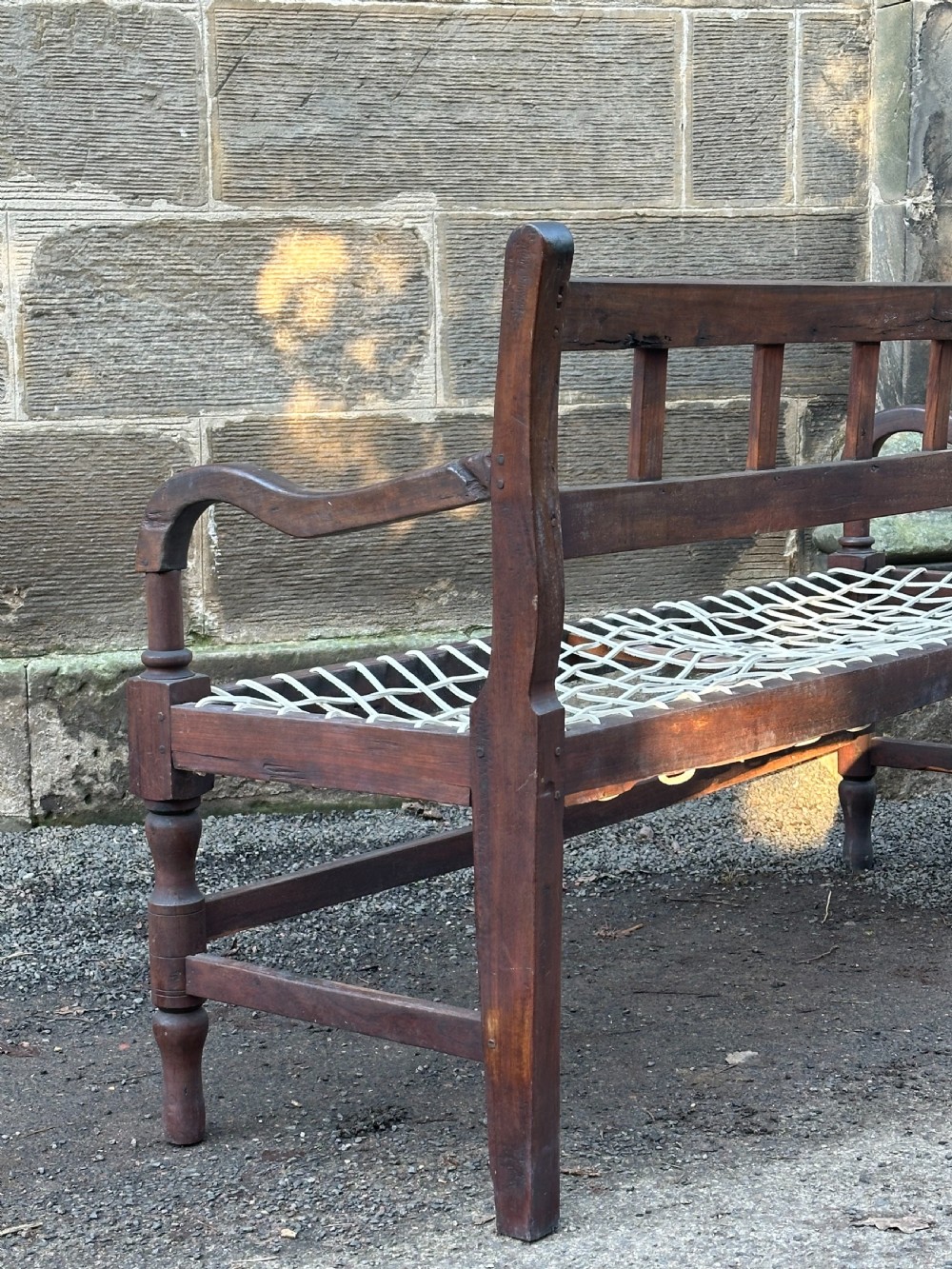 An early 19th-century South African stinkwood bench featuring a woven leather thong seat, curved armrests, and turned front legs. View IV