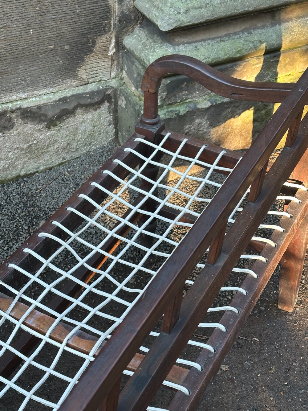 An early 19th-century South African stinkwood bench featuring a woven leather thong seat, curved armrests, and turned front legs. View V