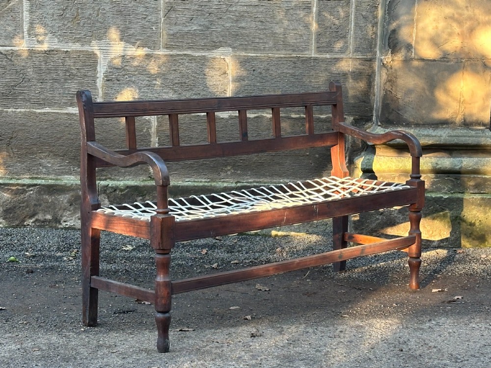 An early 19th-century South African stinkwood bench featuring a woven leather thong seat, curved armrests, and turned front legs.
