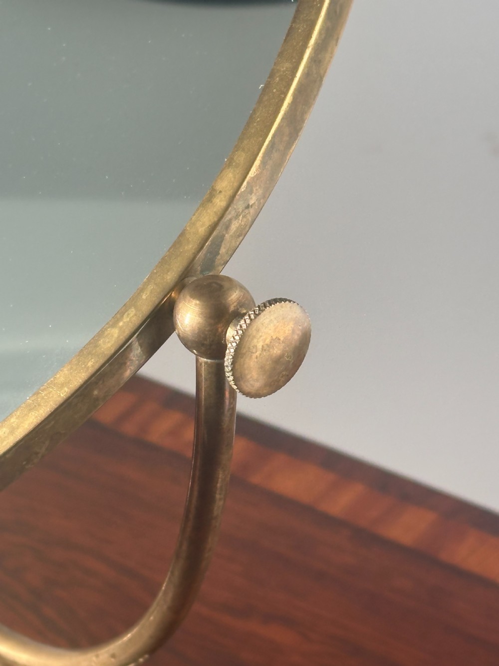 An oval brass shaving mirror on a matching stand sits atop a dark wooden surface. View III