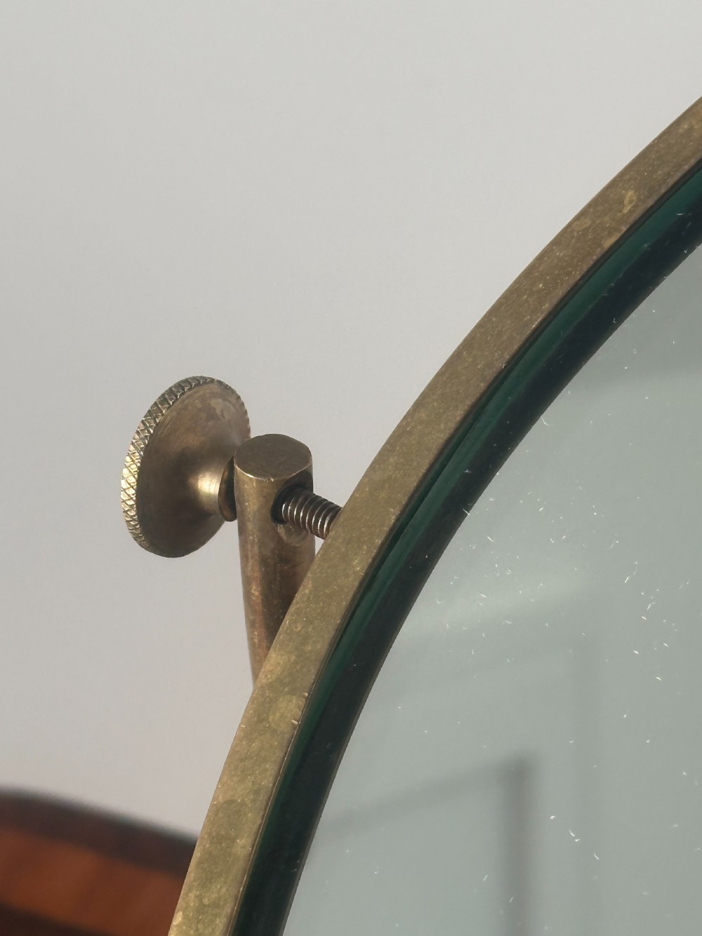 An oval brass shaving mirror on a matching stand sits atop a dark wooden surface. View IV