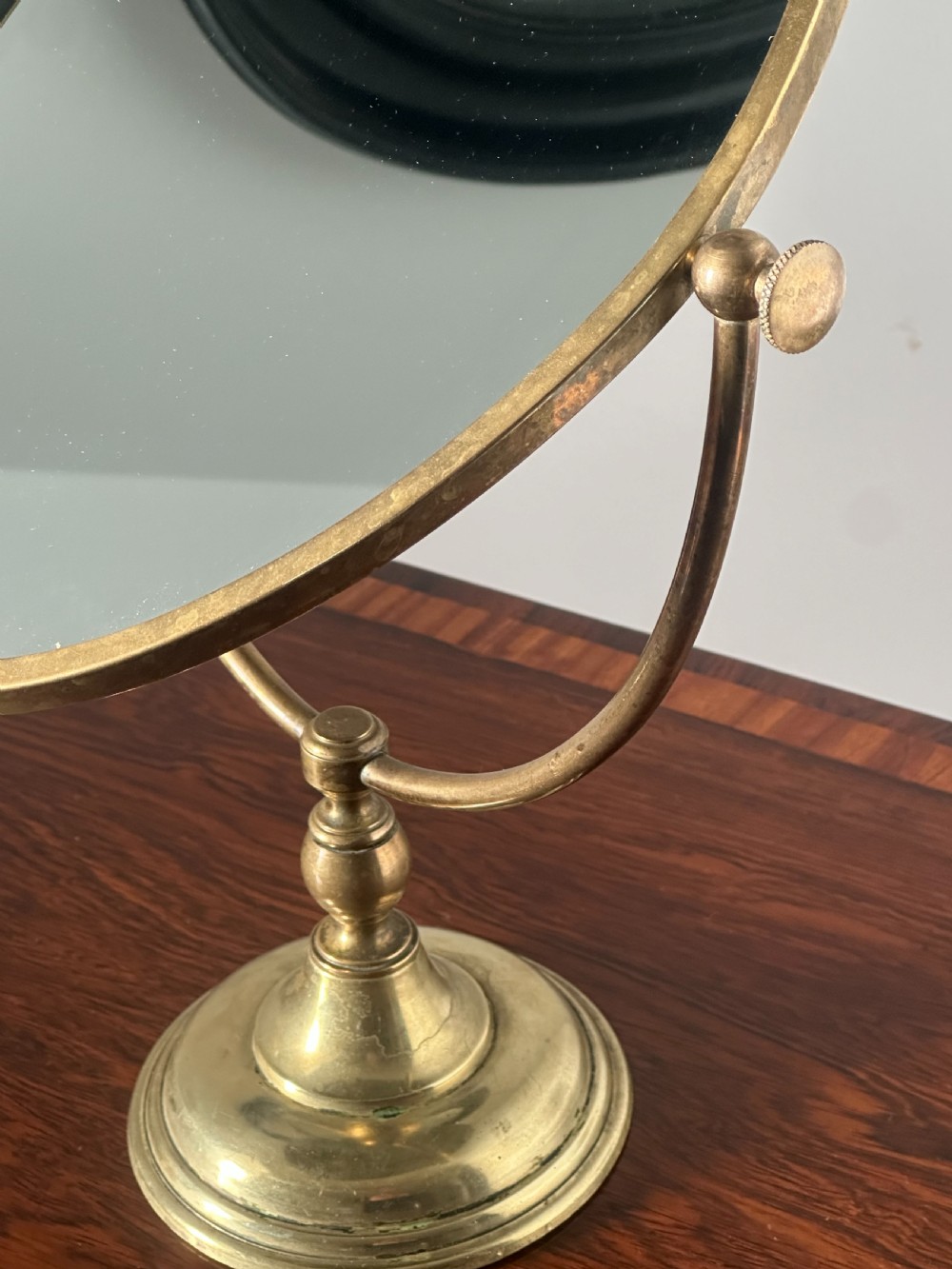 An oval brass shaving mirror on a matching stand sits atop a dark wooden surface. View V