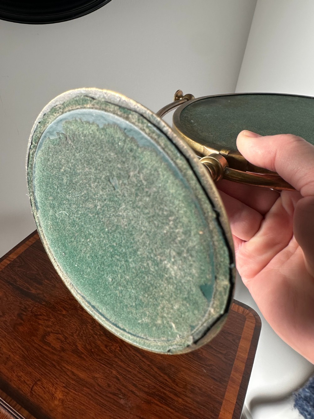 An oval brass shaving mirror on a matching stand sits atop a dark wooden surface. View VIII