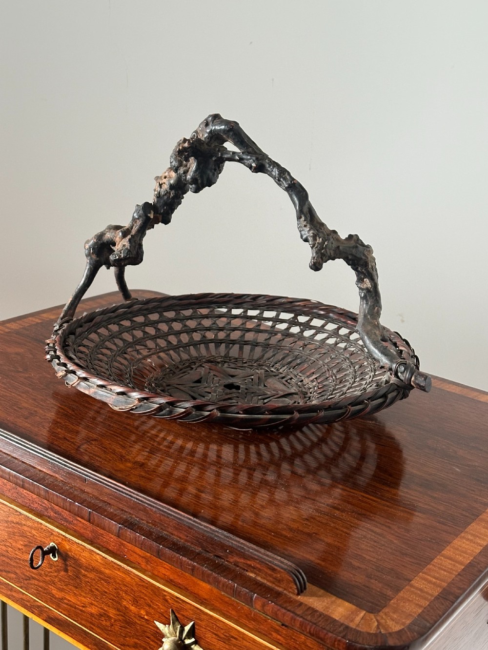 A shallow dark brown woven bamboo Ikebana flower basket featuring an organic gnarled natural rootwood overhead handle. View II