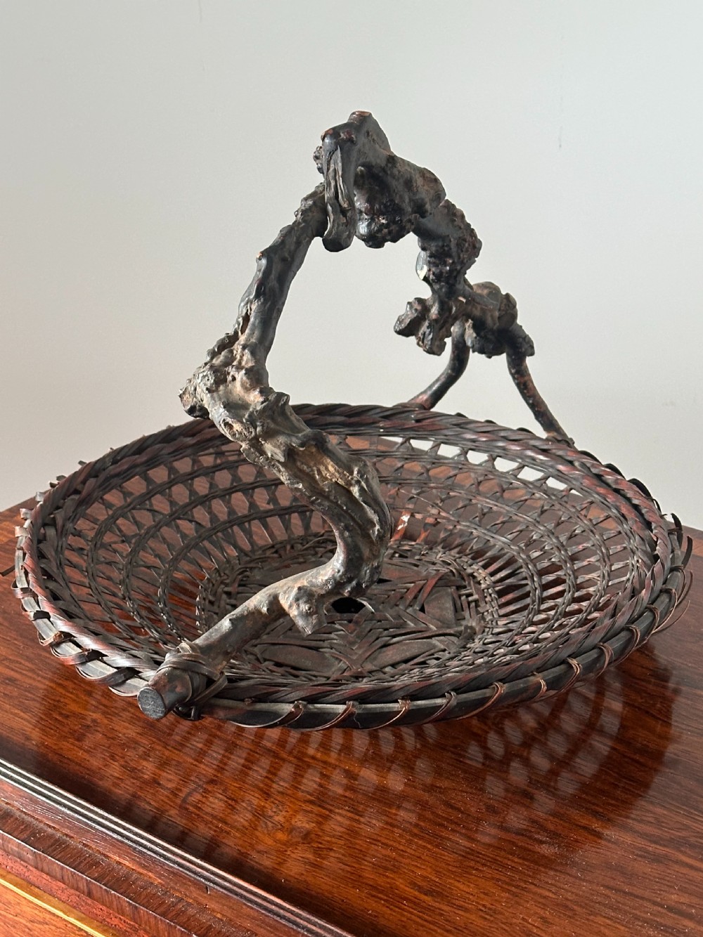 A shallow dark brown woven bamboo Ikebana flower basket featuring an organic gnarled natural rootwood overhead handle. View IV