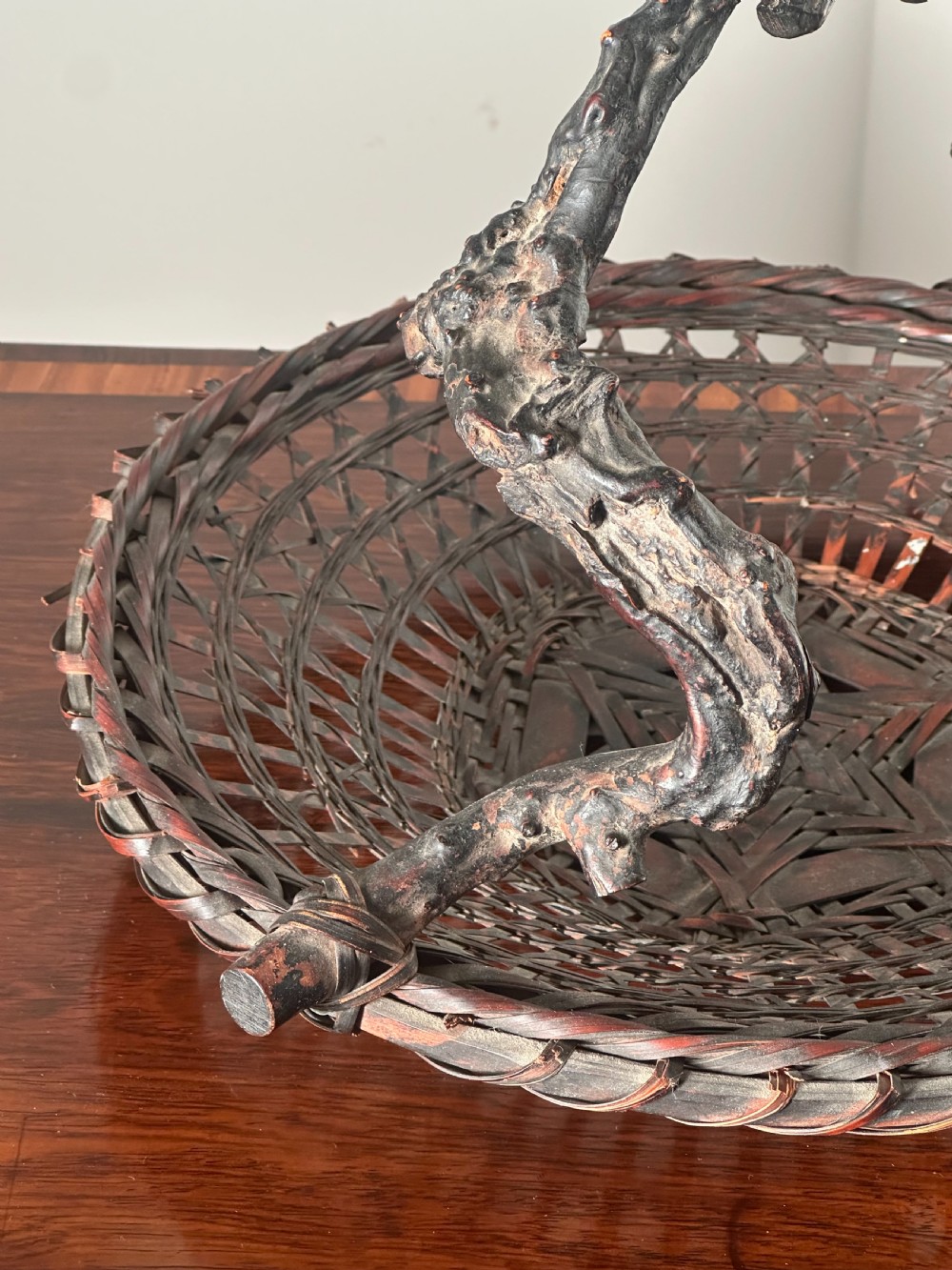 A shallow dark brown woven bamboo Ikebana flower basket featuring an organic gnarled natural rootwood overhead handle. View VI