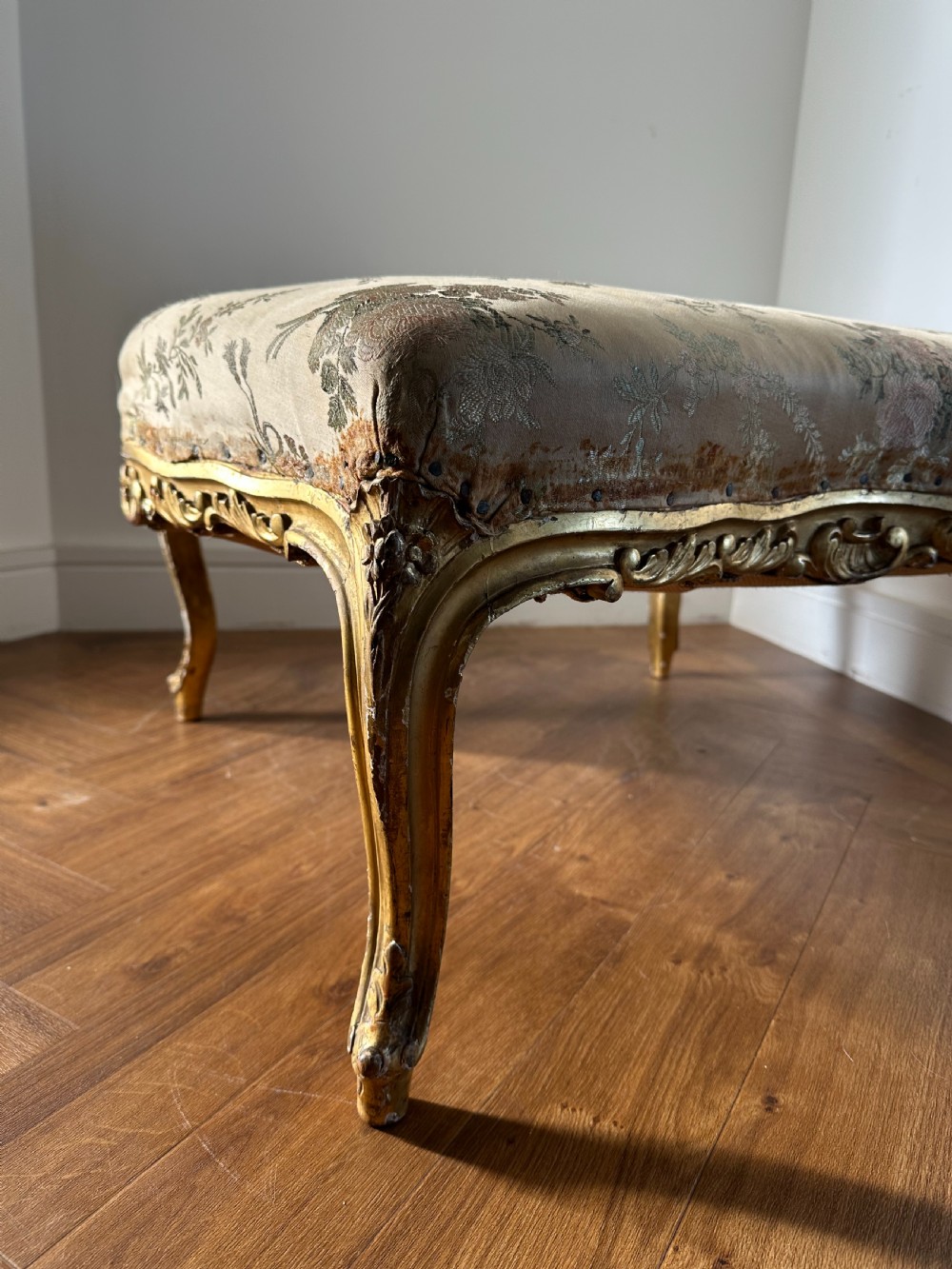 A 19th-century French giltwood centre stool featuring carved Rococo scrollwork, cabriole legs, and floral upholstered seating. View V