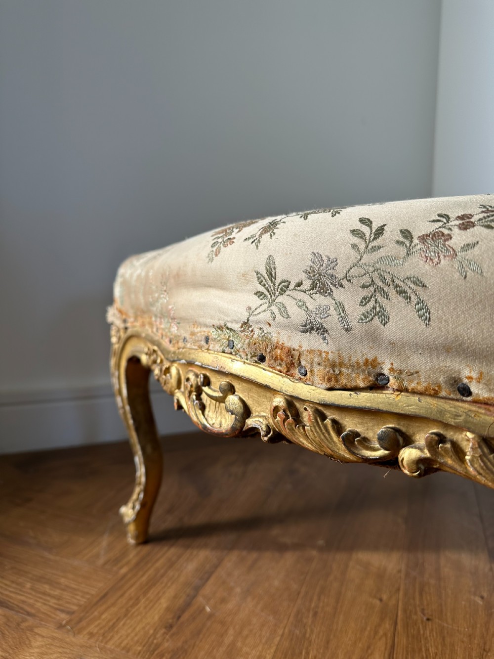 A 19th-century French giltwood centre stool featuring carved Rococo scrollwork, cabriole legs, and floral upholstered seating. View VI