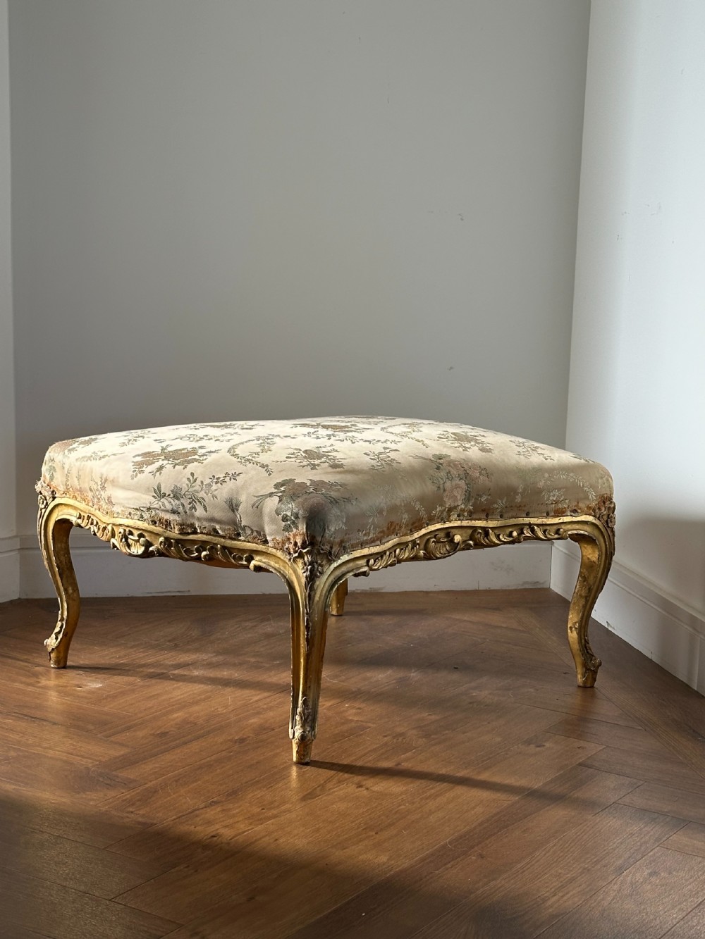 A 19th-century French giltwood centre stool featuring carved Rococo scrollwork, cabriole legs, and floral upholstered seating. View VII