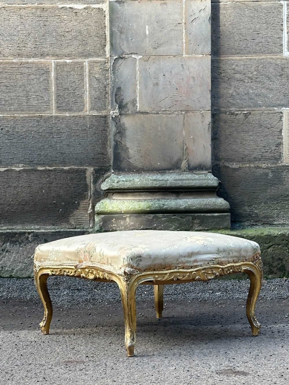 A 19th-century French giltwood centre stool featuring carved Rococo scrollwork, cabriole legs, and floral upholstered seating.
