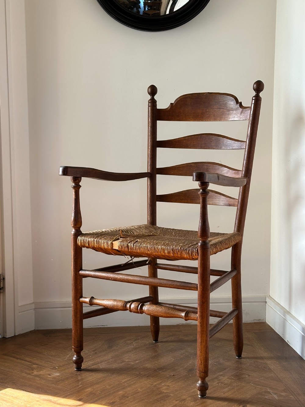 An Anglo-Indian teak wooden armchair with a ladderback rest, turned finials, curved armrests, and a natural woven rush seat.