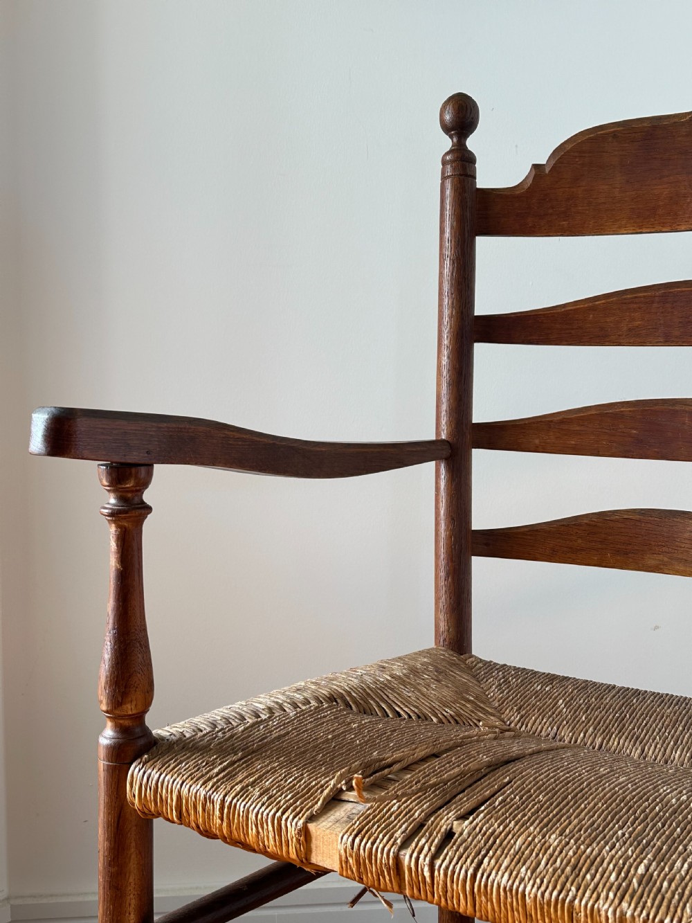 An Anglo-Indian teak wooden armchair with a ladderback rest, turned finials, curved armrests, and a natural woven rush seat. View II