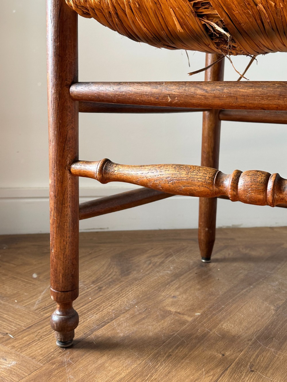 An Anglo-Indian teak wooden armchair with a ladderback rest, turned finials, curved armrests, and a natural woven rush seat. View III