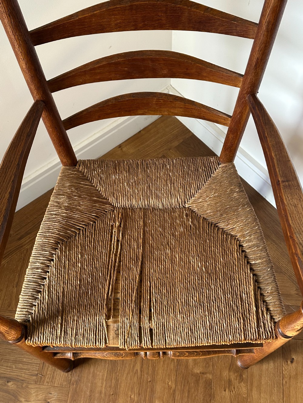 An Anglo-Indian teak wooden armchair with a ladderback rest, turned finials, curved armrests, and a natural woven rush seat. View IV