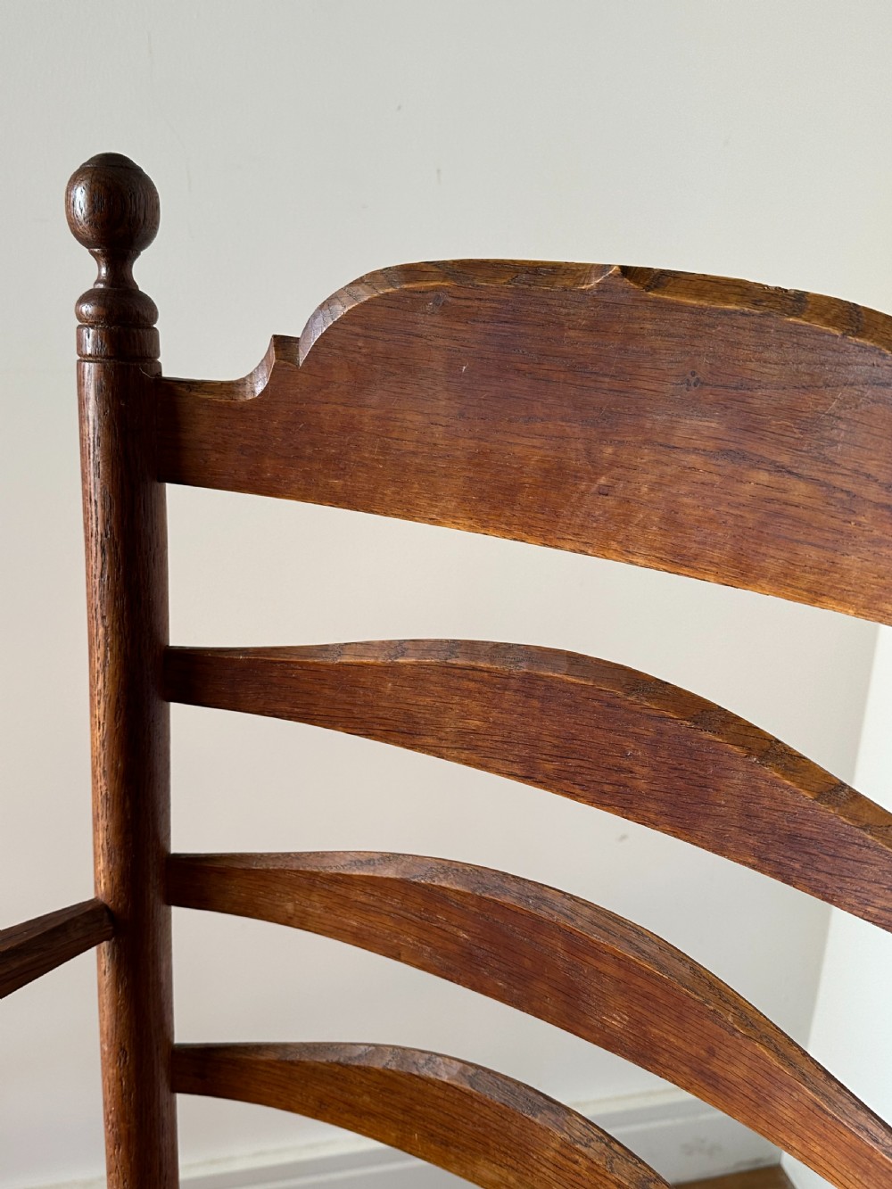 An Anglo-Indian teak wooden armchair with a ladderback rest, turned finials, curved armrests, and a natural woven rush seat. View V