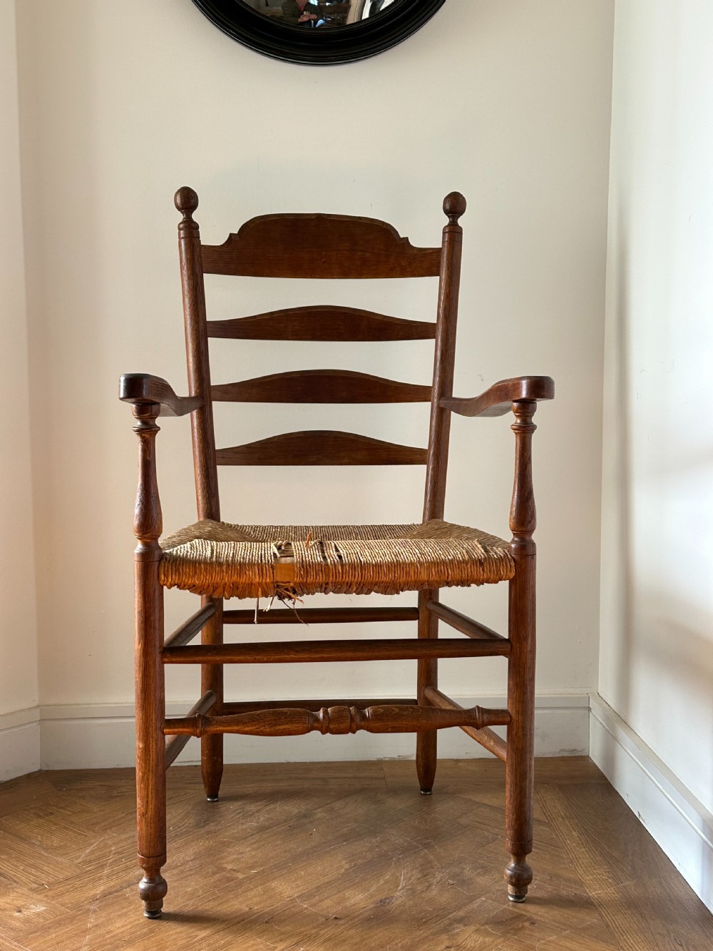 An Anglo-Indian teak wooden armchair with a ladderback rest, turned finials, curved armrests, and a natural woven rush seat. View VI