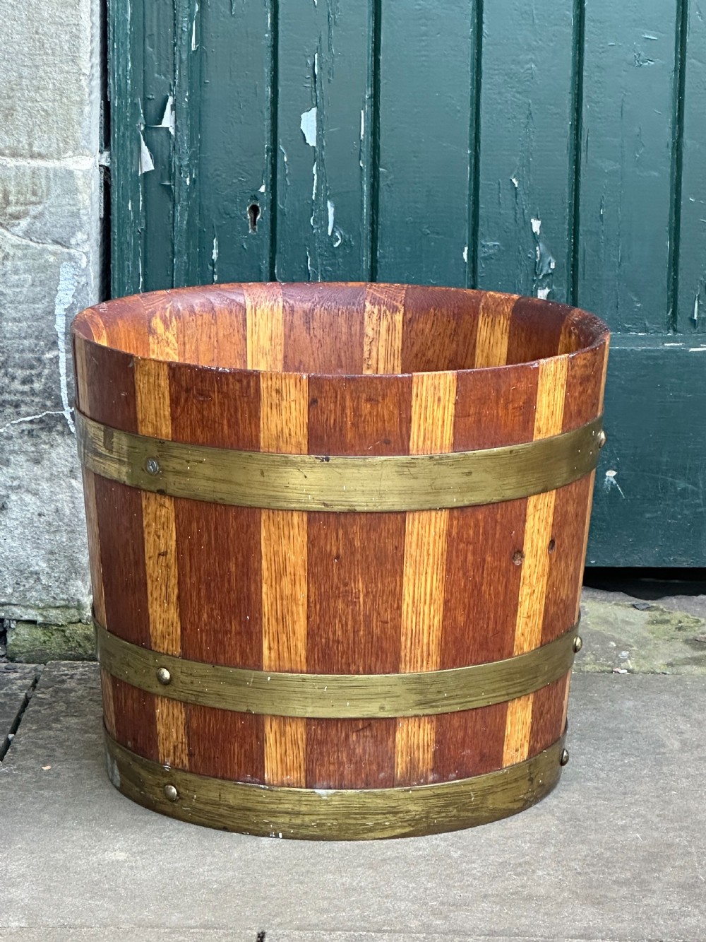 An antique Scottish coopered wooden peat bucket with alternating light and dark staves bound by three brass hoops.