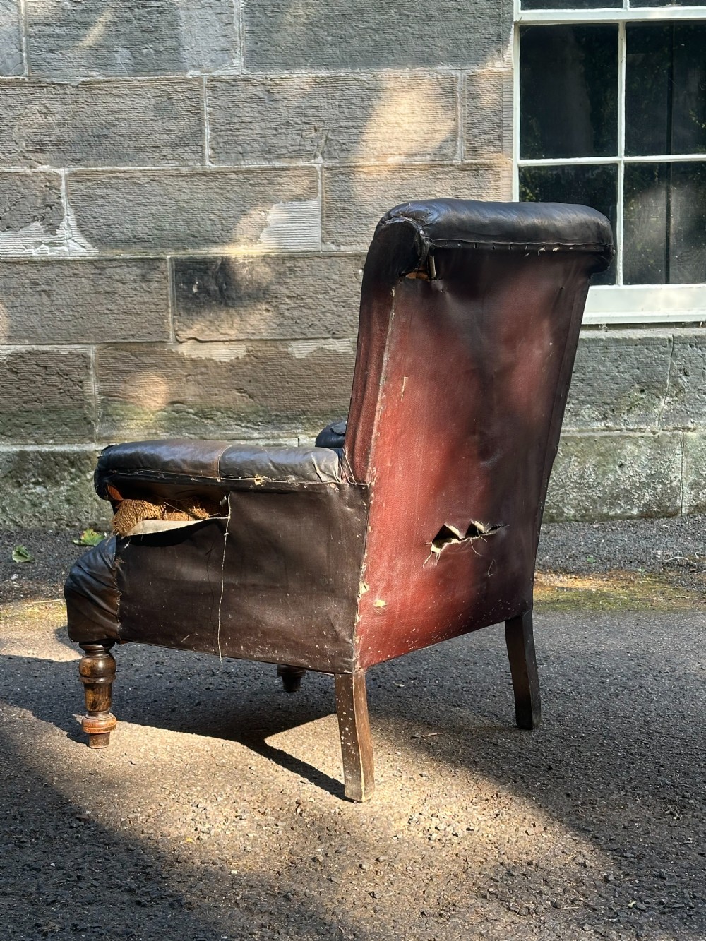 A Victorian library armchair upholstered in worn dark brown leather featuring a buttoned backrest, padded arms, and turned wooden front legs. View IV