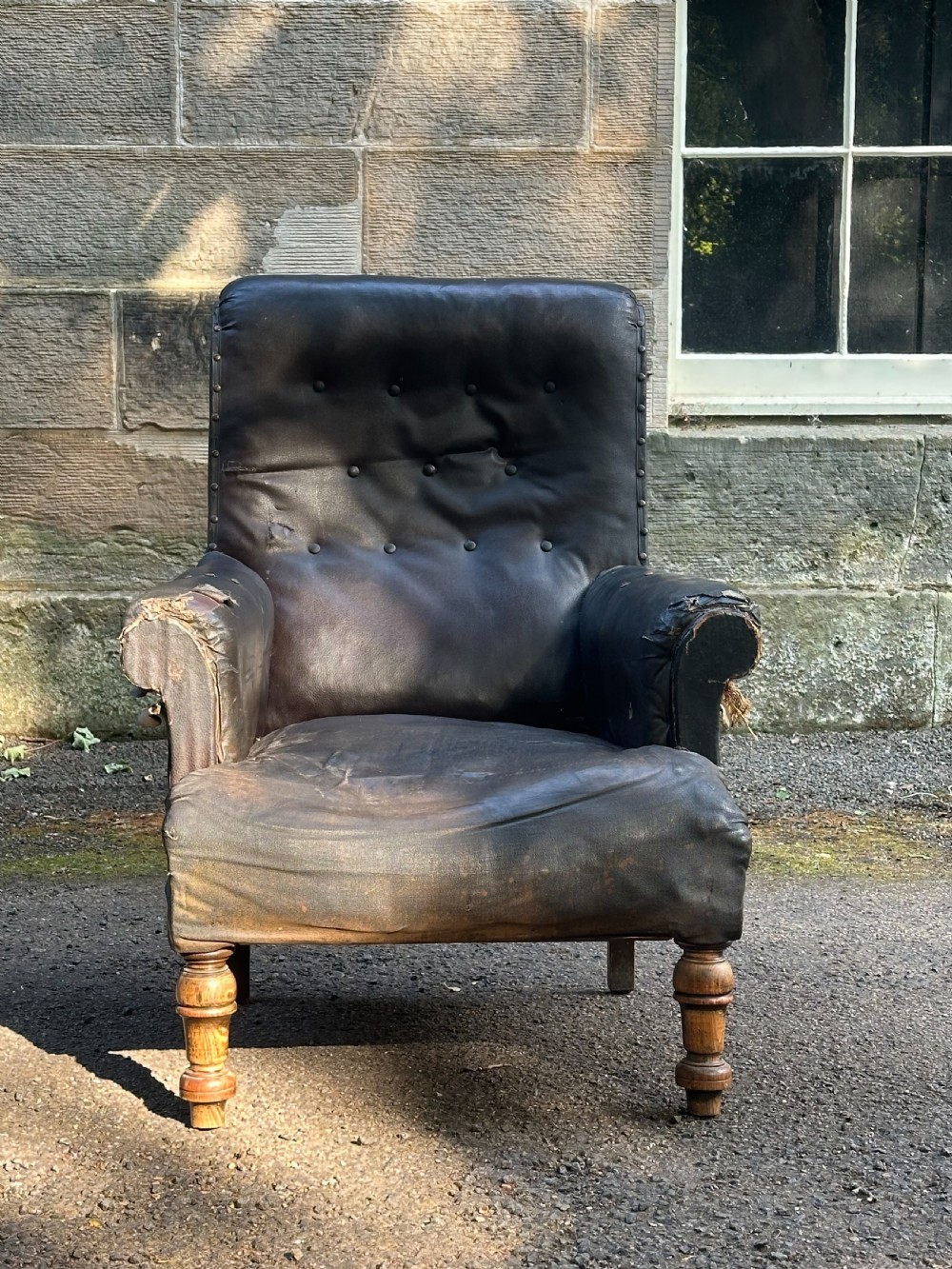 A Victorian library armchair upholstered in worn dark brown leather featuring a buttoned backrest, padded arms, and turned wooden front legs.