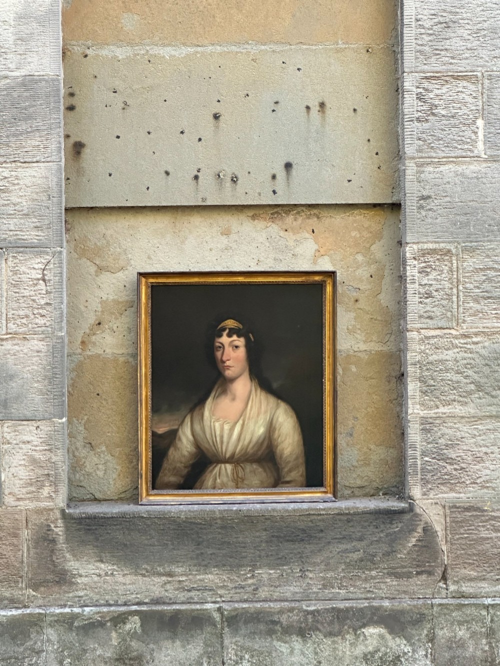 An early nineteenth-century portrait painting on canvas showing a woman in a cream Empire-line dress framed in carved gold leaf wood. View II