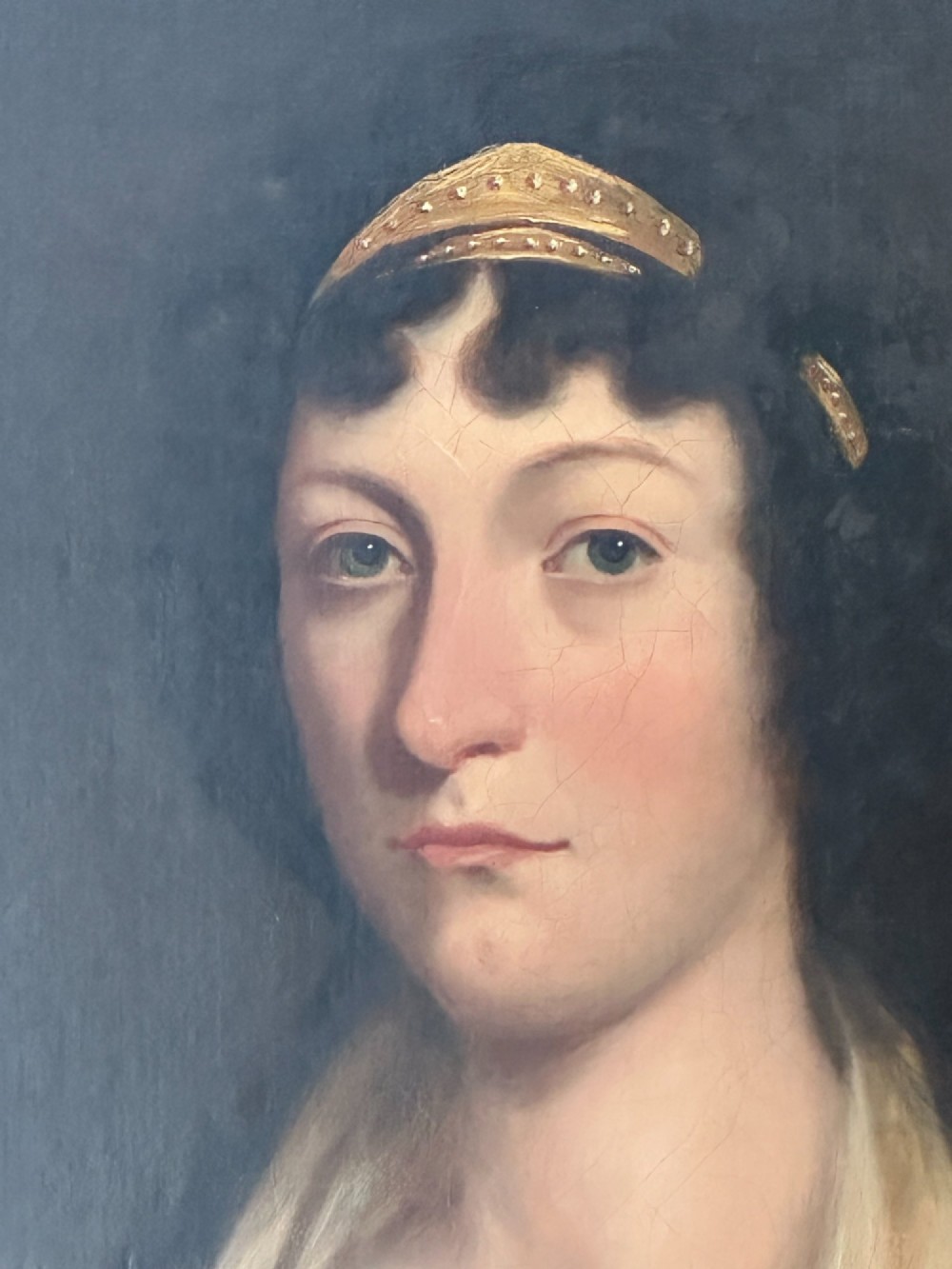 An early nineteenth-century portrait painting on canvas showing a woman in a cream Empire-line dress framed in carved gold leaf wood. View IV