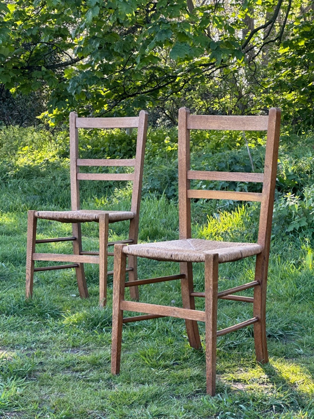 A pair of Arts and Crafts oak and rush seated chairs in the manner of Heals