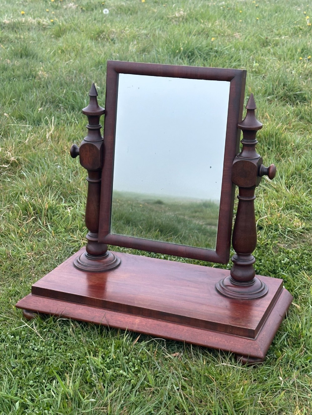 A mid-19th century mahogany dressing mirror featuring turned side supports, finials, and a moulded rectangular plinth base. View II