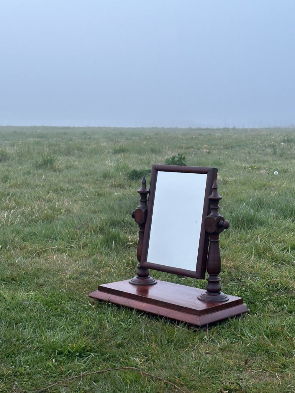 A mid-19th century mahogany dressing mirror featuring turned side supports, finials, and a moulded rectangular plinth base.