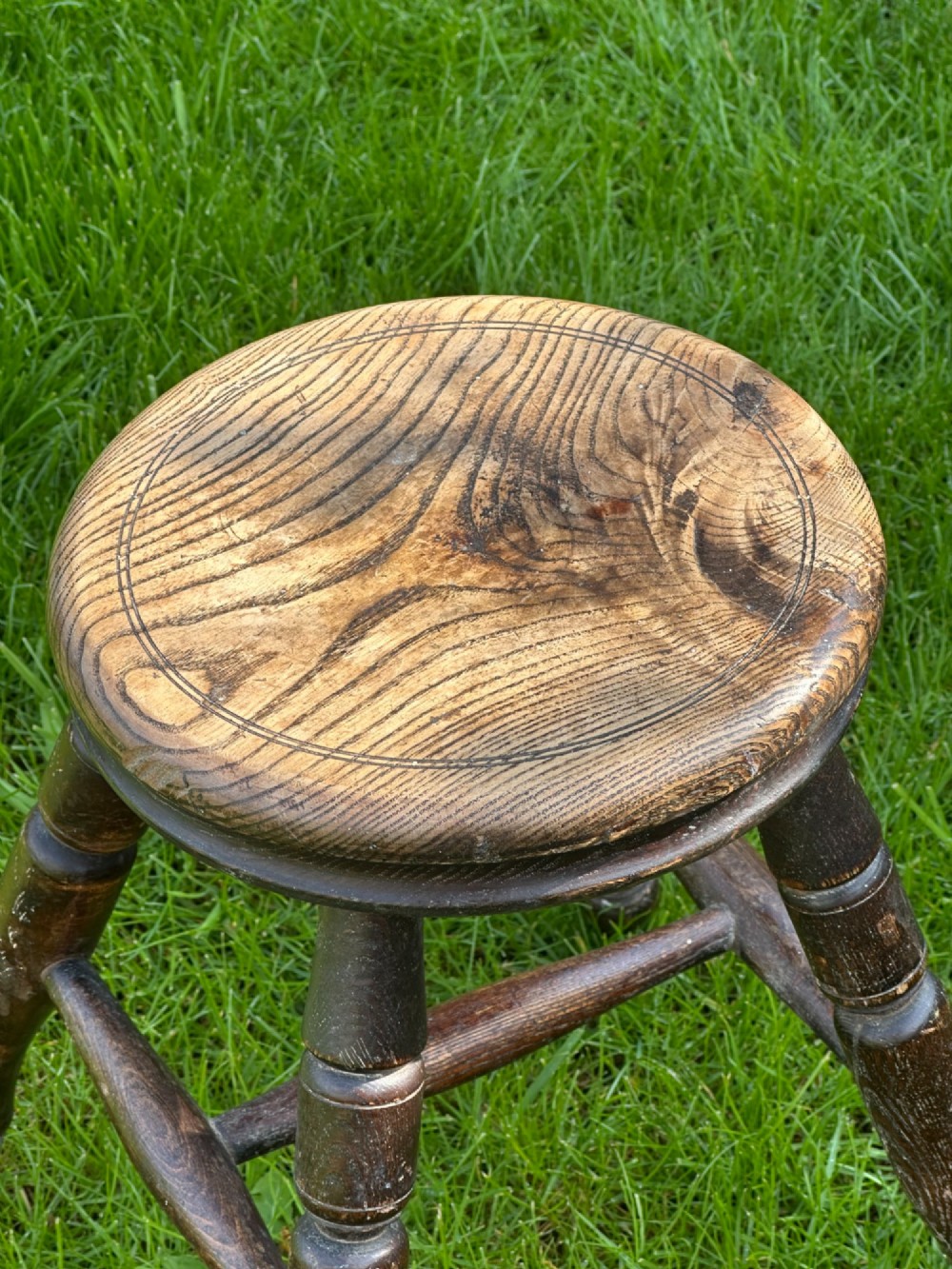 A 19th-century rustic wooden stool featuring a circular solid elm seat and four dark turned splayed legs with stretchers. View III