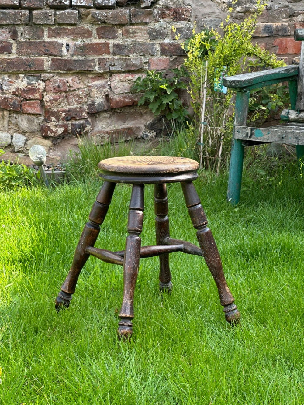 A 19th-century rustic wooden stool featuring a circular solid elm seat and four dark turned splayed legs with stretchers.